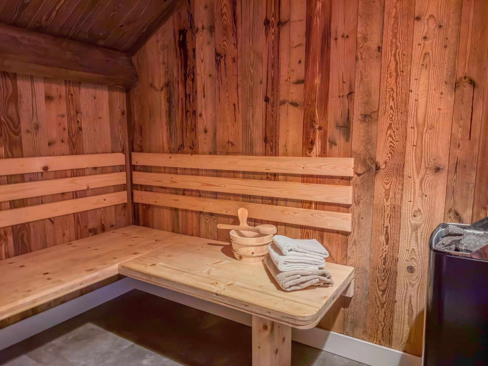Private wooden sauna with L-shaped benches, folded towels, bucket and ladle