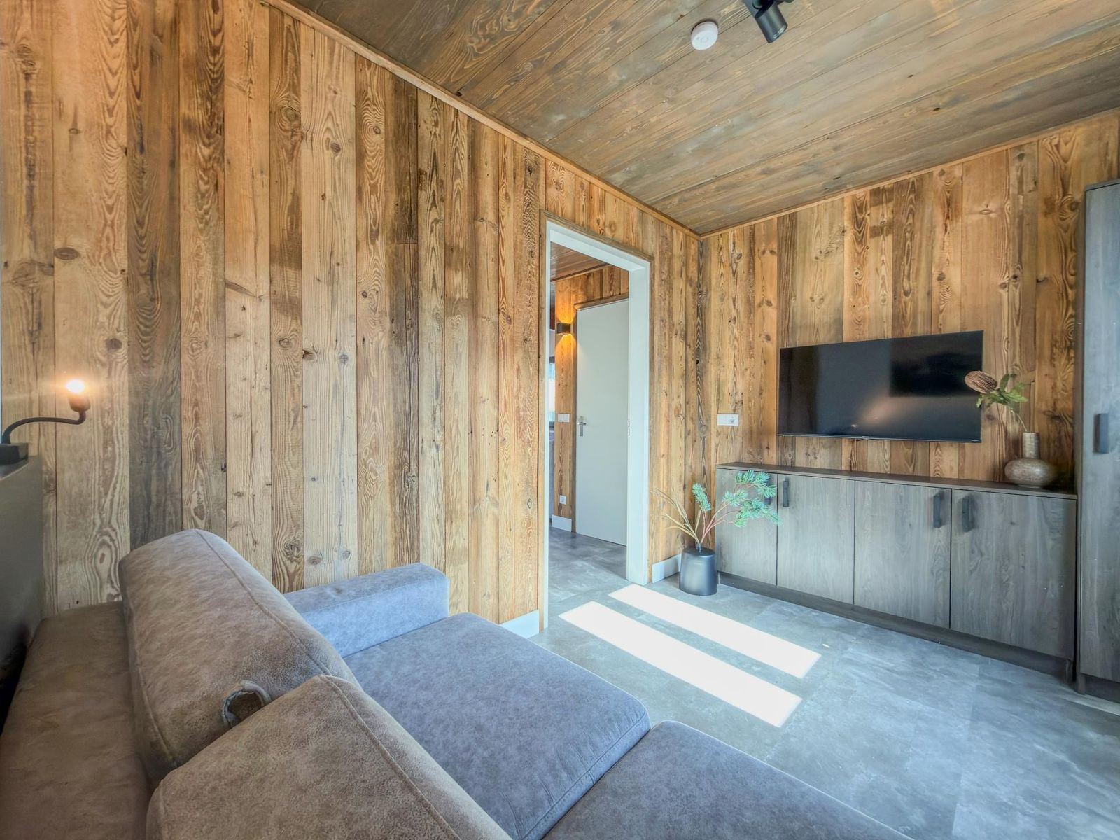 Living area with grey sofa, timber feature wall and television in soft sunlight