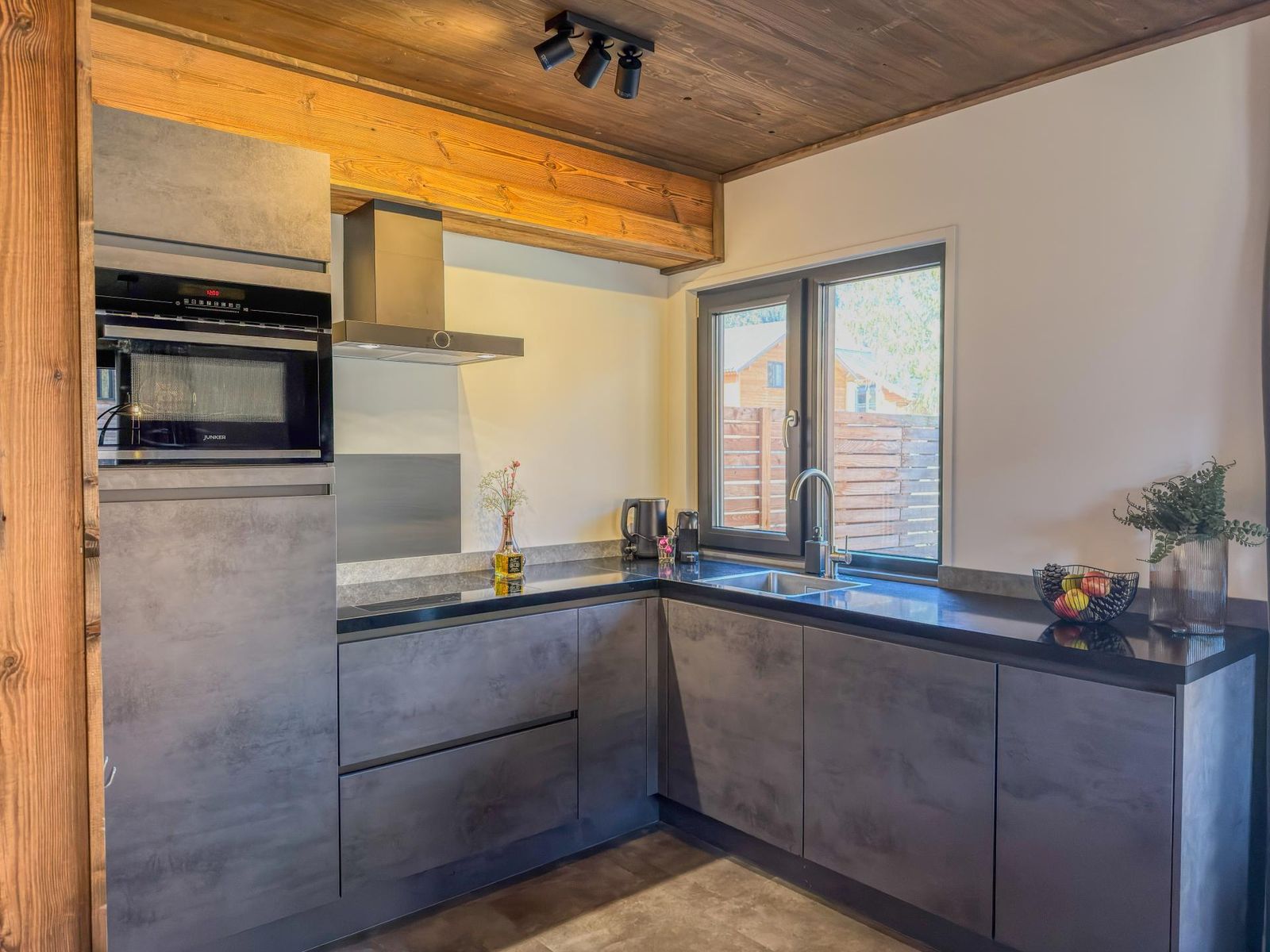 Dark-grey fitted kitchen with oven, microwave, hob and window above the sink