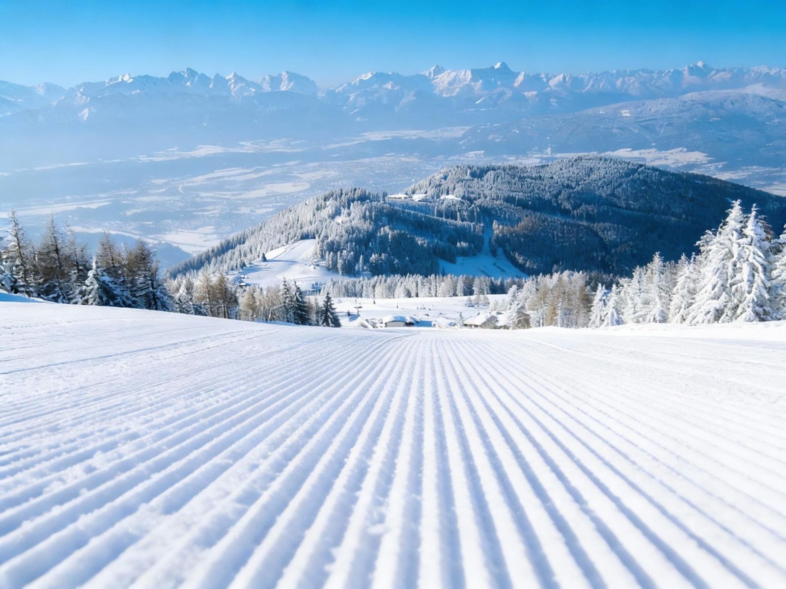 Groomed ski slope with snow-covered trees and a wide mountain panorama
