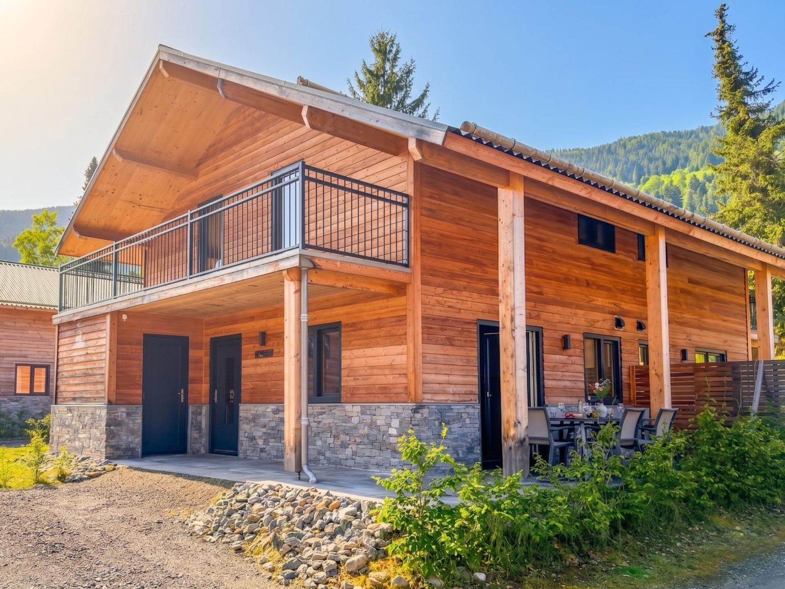 Wood and stone vacation home with balcony and covered terrace against a forested mountainside