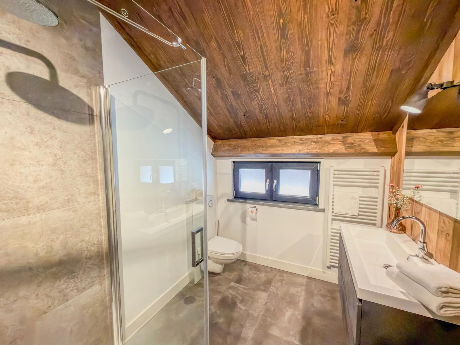 Bathroom with glass shower, vanity and towel rail under a sloped wooden ceiling