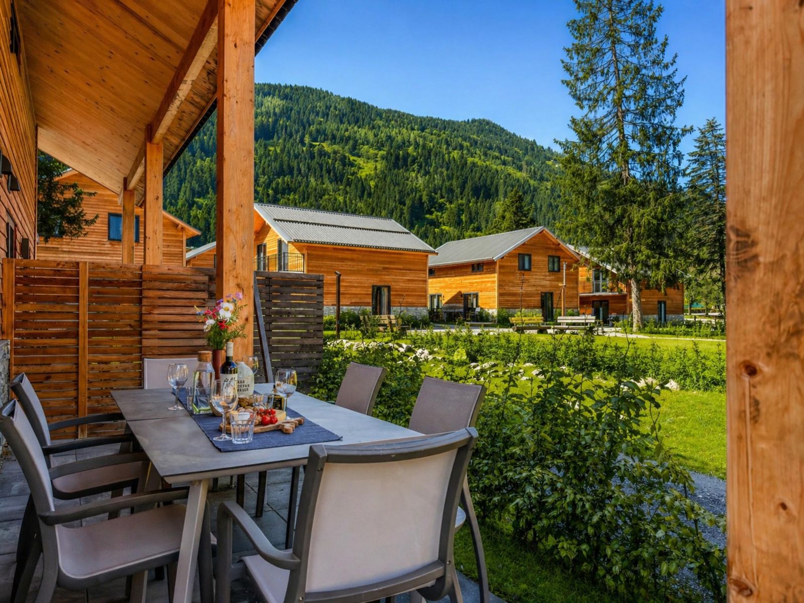 Covered terrace with a set dining table, hedge screening and mountain greenery beyond