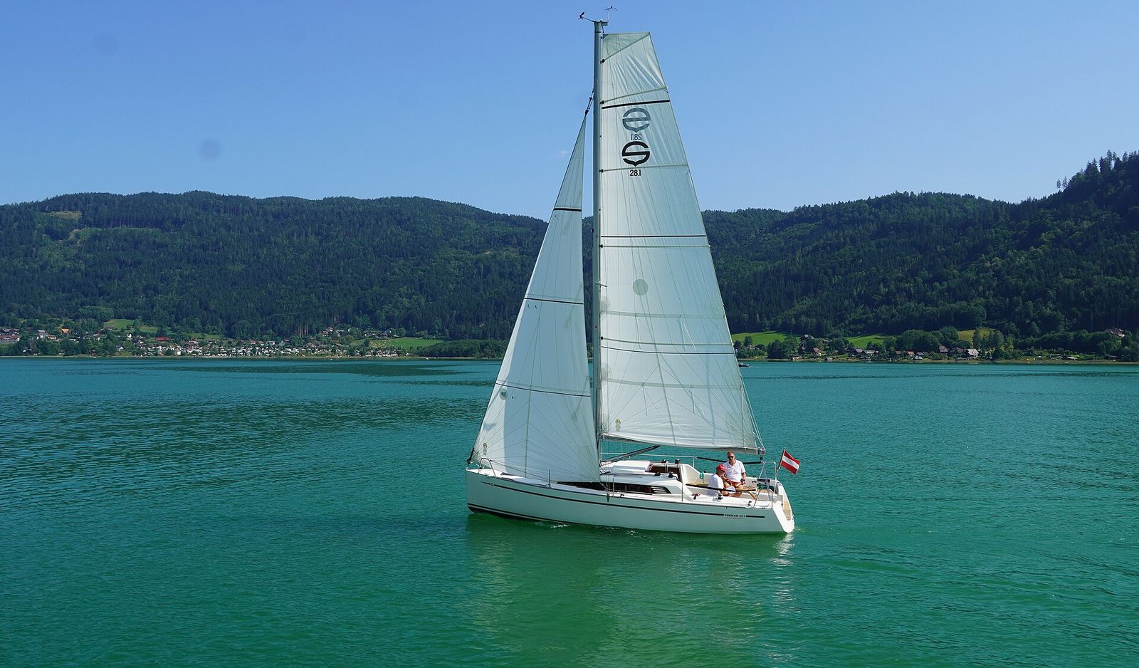 White sailing boat on the turquoise Ossiacher See with wooded shore behind